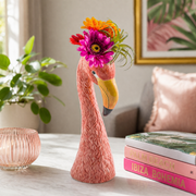 Pink ceramic flamingo vase with textured body, filled with colorful flowers and leaves